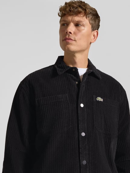 Männermodel trägt Regular Fit Hose mit seitlichen Eingrifftaschen von Lacoste in unifarbener Cord-Struktur, Nahaufnahme Oberkörper.