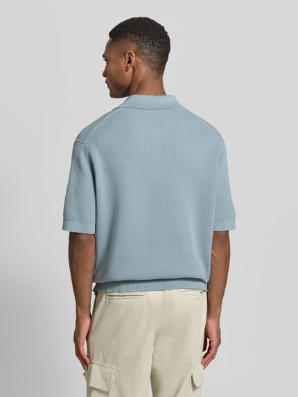 Männermodel trägt Relaxed Fit Poloshirt aus reiner Baumwolle Modell 'DANE' von SELECTED HOMME in Hellblau mit Strickoptik, Ganzkörperansicht Rückansicht.