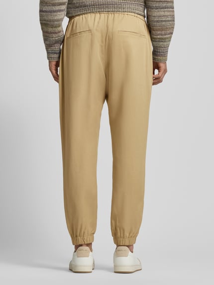 Männermodel trägt Loose Fit Stoffhose aus Lyocell-Leinen-Mix von Antony Morato in Beige mit elastischem Bund, Gesäßtaschen, Ganzkörperansicht Rückansicht.