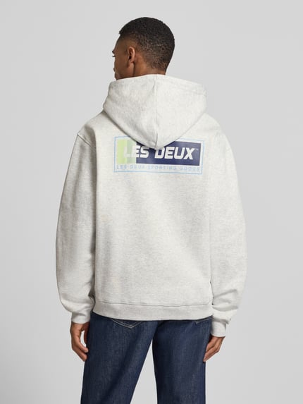 Männermodel trägt Hoodie mit Logo-Print Modell 'Chase' von Les Deux aus grauer Baumwolle, Loose Fit, Rückansicht, Ganzkörperansicht.