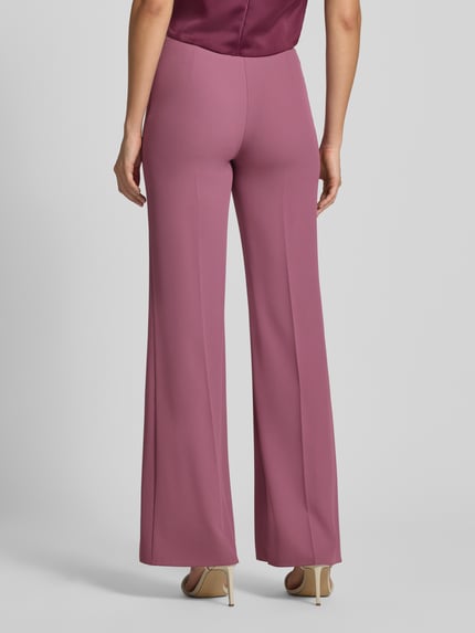 Kobiece modelka nosi spodnie Flared Fit Hose mit Bundfalten von Rinascimento w różowym kolorze, elastyczna mieszanka materiałów, rozkloszowany krój, elastyczny pas, wszyty zamek błyskawiczny, szerokość w rozmiarze S: 37 cm, długość wewnętrzna nogawki w rozmiarze S: 85 cm, widok całej sylwetki od tyłu