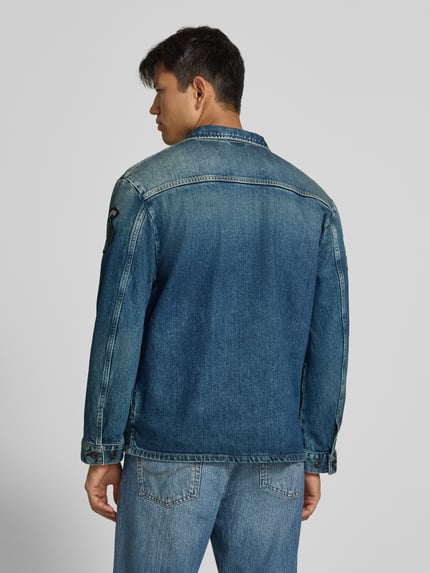 Männermodel trägt Regular Fit jeansjack van katoenmix met all-over labelpatches van Replay, borstzak, steekzakken, platte kraag, knoopsluiting, ruglengte maat M 70 cm, schouderbreedte 48 cm, borstwijdte 55 cm, mouwlengte 66 cm, Ganzkörperansicht Rückansicht.