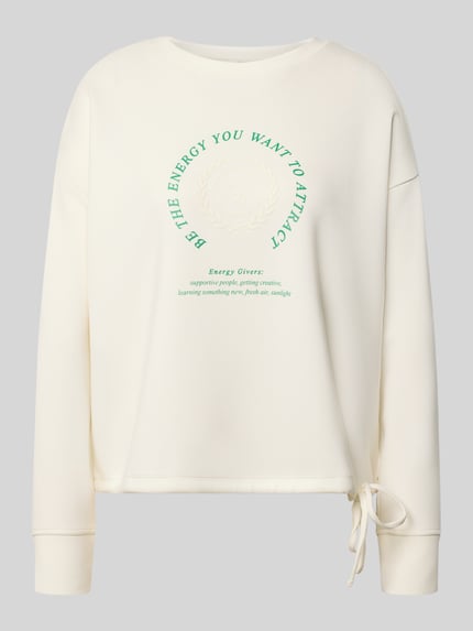 Frauenmodel trägt Sweatshirt mit Bändel und Frontprint von Christian Berg Woman w kolorze kremowym, mieszanka modalu, krój oversized, okrągły dekolt, nadruk z przodu, detal taśmy do wiązania, Ganzkörperansicht von vorne.