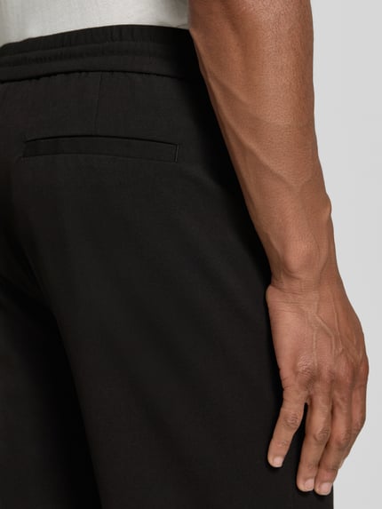 Männermodel trägt Relaxed Fit Sweatpants mit Viskose-Anteil von Lindbergh in Schwarz, Elastischer-Material-Mix, Detailaufnahme Rückansicht. Bundweite bei Größe M: 41 cm, Innenbeinlänge bei Größe M: 79 cm, Bügelfalten, elastischer Bund mit Tunnelzug.