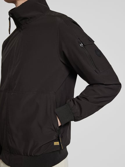 Männermodel trägt schwarzen Windbreaker mit Stehkragen Modell 'YETUR' von CARS JEANS, Reißverschlusstasche am Arm, Nahaufnahme Oberkörper.
