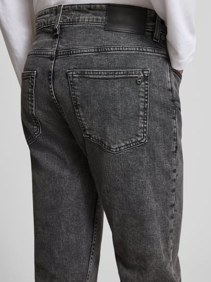 Męski model nosi Straight Fit Jeans aus Baumwoll-Mix Modell 'DELAWARE BO' od BOSS Orange, melanżowy denim, 5 kieszeni, widok z tyłu.