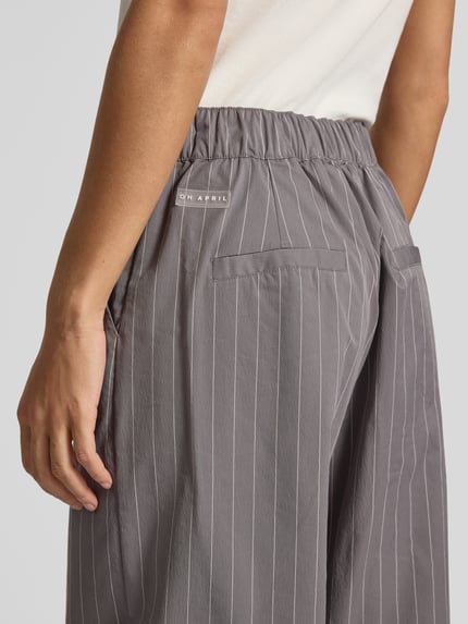 Frauenmodel trägt Barrel Fit Hose mit Eingrifftaschen Modell 'Zoya' von OH APRIL, grau mit weißen Streifen, Material-Mix, Nahaufnahme Hüfte, KI-modifiziertes Bild.