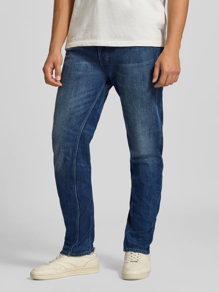 Männermodel trägt blaue, leicht verwaschene Tapered Fit Jeans aus reiner Baumwolle Modell 'G-Star Arc' von G-Star RAW, Nahaufnahme Unterkörper.