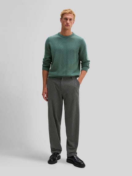 Männermodel trägt Pullover mit Logo-Detail von MARC O'POLO in grün-melierter Strickoptik, Struktur-Muster, Regular Fit, Ganzkörperansicht von vorne.