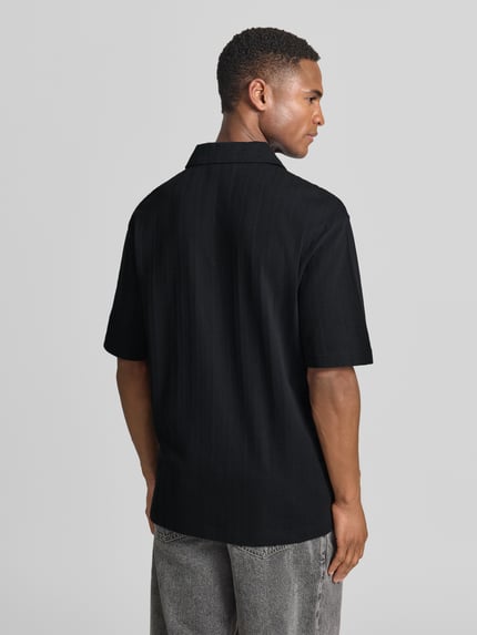 Männermodel trägt Relaxed Fit Poloshirt mit Strukturmuster Modell 'DALIBO' von HUGO, Optik: Unifarben, reine Baumwolle, Ganzkörperansicht Rückansicht.