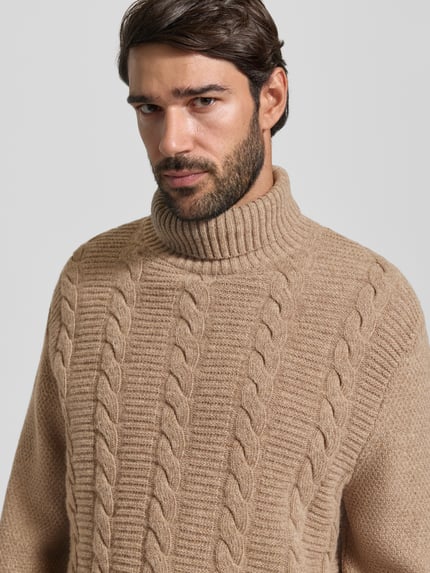 Męski model nosi Pullover aus Wolle mit Rollkragen od BARBOUR, brązowy sweter z czystej wełny, strukturalny wzór, długi rękaw, wykończenia prążkowane, dzianina, zbliżenie na górną część ciała.