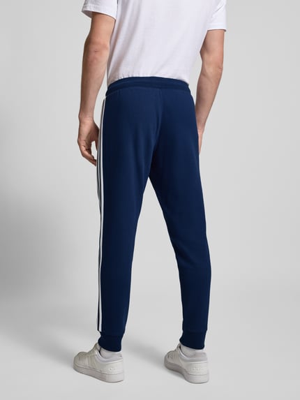 Männermodel trägt Spodnie dresowe mit elastycznym pasem od adidas Originals, mieszanka bawełny, luźny krój, wpuszczane kieszenie, wyhaftowane logo, długość wewnętrzna nogawki 38 cm przy rozmiarze M, widok całej sylwetki od tyłu.