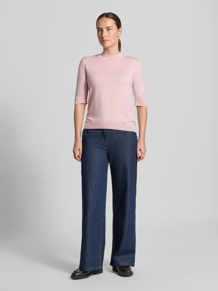 Frauenmodel trägt Strickpullover aus Viskose-Mix von MORE & MORE in Rosa mit Stehkragen, taillierte Passform, Ganzkörperansicht von vorne.