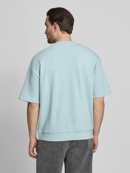 Männermodel trägt Oversized T-Shirt mit Rundhalsausschnitt von Lindbergh, Baumwoll-Mix, Label-Detail, Rückenlänge 70 cm, Ganzkörperansicht Rückansicht.