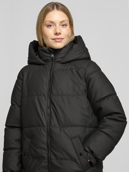 Frauenmodel trägt schwarzen, unifarbenen Puffer Coat mit Kapuze von VERO MODA, Struktur, Label-Detail, Regular Fit, Nahaufnahme Oberkörper.