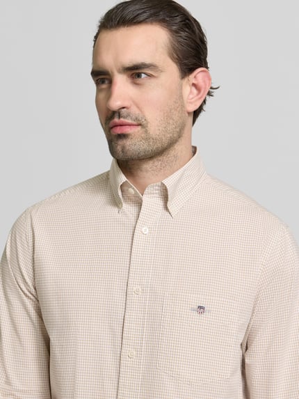 Männermodel trägt Slim Fit Freizeithemd mit Logo-Stitching von Gant in Beige mit feinem Karo, reine Baumwolle, Nahaufnahme Oberkörper.