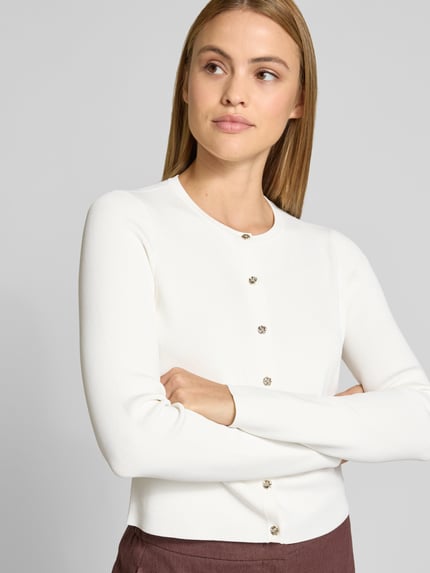Frauenmodel trägt weißen Slim Fit Cardigan aus Viskose-Mix Modell 'Velda' von Ted Baker mit Strick-Optik, Langärmelig, Rundhalsausschnitt, durchgängige Knopfleiste, Nahaufnahme Oberkörper, Rückenlänge bei Größe 36: 47 cm, Ärmellänge bei Größe 36: 63 cm.