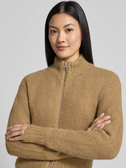 Frauenmodel trägt Regular Fit Jacke aus Alpaka-Mix Modell 'Jeanne' von Samsøe Samsøe in beige Strick-Optik, Nahaufnahme Oberkörper. Elastischer Stoff, Stehkragen und Zweiwege-Reißverschluss.