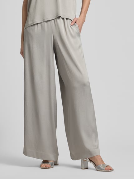 Frauenmodel trägt Loose Fit Stoffhose mit Stretch-Anteil von Drykorn aus Acetat-Elasthan-Mix in hellem Grau, weites Bein, Elastikbund, Nahaufnahme Unterkörper.