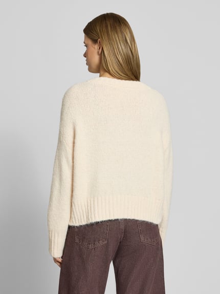 Frauenmodel trägt Pullover mit tiefem V-Ausschnitt von ONLY in Creme mit weicher Strickstruktur, Ganzkörperansicht Rückansicht. Damen Pullover von ONLY.