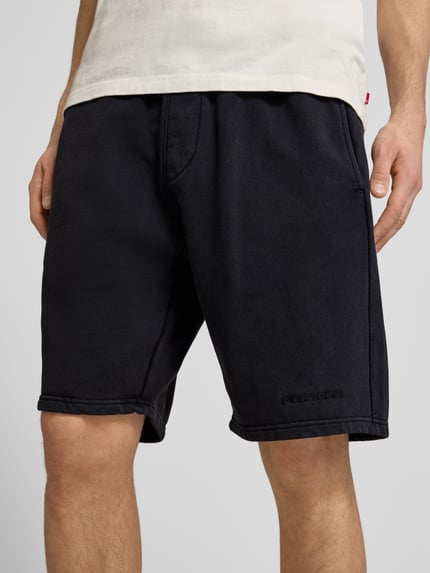 Männermodel trägt Shorts mit elastischem Bund und Logo-Stitching von Pegador, Schwarz, Baumwoll-Mix, Loose-Fit, Nahaufnahme Oberschenkel.