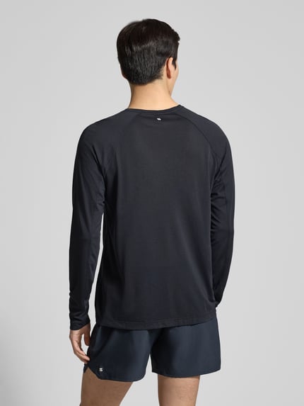 Męski model nosi Funktionsshirt mit Logo und Rundhalsausschnitt von Salomon, krój regular fit, czarny, długi rękaw, widok całej sylwetki z tyłu.