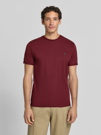 Männermodel trägt T-Shirt mit Logo-Stitching und Rundhalsausschnitt von Les Deux, Baumwoll-Mix mit Stretch-Anteil, Straight Fit, Ganzkörperansicht von vorne.