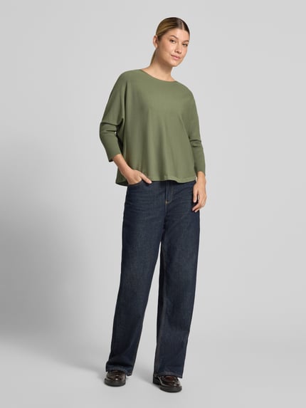 Frauenmodel trägt Strickpullover aus Viskose-Mix Modell 'Tiraja' von someday. in Olivgrün, Relaxed Fit, Rundhalsausschnitt, 3/4-Arm, kombiniert mit dunkler Jeans, glatte Textur, Ganzkörperansicht von vorne.
