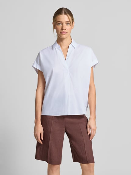 Frauenmodel trägt Regular Fit Bluse mit V-Ausschnitt Modell 'Basilia' von JOOP!, weiß, Baumwoll-Mix mit Stretch-Anteil, Hemdblusenkragen, Ärmel mit Aufschlag, Rückenlänge 62 cm, Ärmellänge 3 cm, Ganzkörperansicht von vorne.