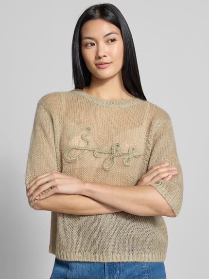 Frauenmodel trägt Regular Fit Pullover aus Schurwoll-Modal-Mix Modell 'C_Farezza' von BOSS für Damen von BOSS Orange in Beige mit grober Strickstruktur und gesticktem Logo, Nahaufnahme Oberkörper.