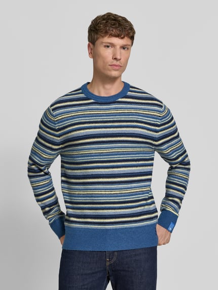 Männermodel trägt Regular Fit Strickpullover mit Streifen-Muster von Scotch & Soda, Mieszanka materiałów z dodatkiem wełny, krój regular fit, wzór w paski, elastyczne wykończenia, długość tyłu w rozmiarze M: 70 cm, długość rękawów w rozmiarze M: 69 cm, Ganzkörperansicht von vorne