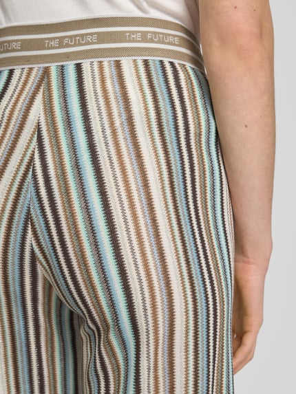Vrouwenmodel draagt Straight Fit Stoffhose mit Viskose-Anteil Modell 'Allison' van Cambio, gestreept in bruin, blauw en beige, elastische tailleband met statement-stitching, modal-mix in breilook, detailopname achterzijde.