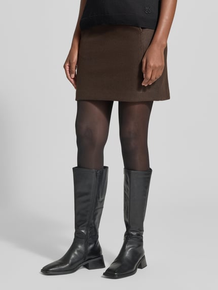 Frauenmodel trägt Ausgestellter Mini-Rock mit Nahtreißverschluss Modell 'FORTUNEALLISON' von VERO MODA in Braun, schwarze Strumpfhose und Stiefel, Nahaufnahme Unterkörper, Damen Mini-Rock von VERO MODA.