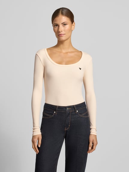 Frauenmodel trägt Longsleeve in Ripp-Optik Modell 'COLETTE' von GUESS Activewear, Slim Fit, Viskose-Elasthan-Mix, Rundhalsausschnitt, dezentes Label-Detail, helle Farbe, feine Struktur, Ganzkörperansicht von vorne.