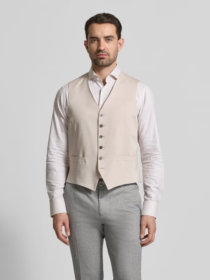 Männermodel trägt Regular Fit Weste aus Viskose-Mix mit V-Ausschnitt von JOOP! Collection in Beige, Knopfleiste und Eingrifftaschen, Kombination mit hellgrauer Hose und weißem Hemd, elastischer Mix mit Baumwoll-Anteil, Ganzkörperansicht von vorne.