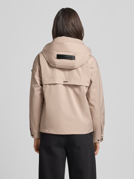 Vrouwenmodel draagt Jacke mit Stehkragen van khujo in beige met opstaande kraag, ritssluiting, ritszakken, regular fit, ruglengte maat S 60 cm, schouderbreedte 51 cm, borstwijdte 50 cm, mouwlengte 54 cm, geheel van achteren.