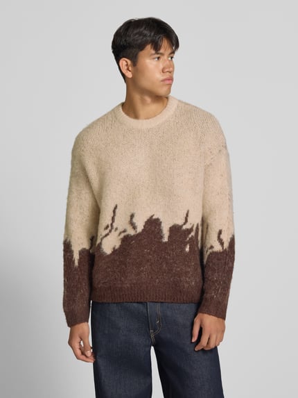 Männermodel trägt Strickpullover mit gerippten Abschlüssen von ANOTHER COTTON LAB, beige-braune Farben, lockere Struktur, ganzkörperansicht von vorne. Elastischer Material-Mix mit Lanawoll-Anteil, gerader Schnitt, Rundhalsausschnitt, überschnittene Ärmel, Rückenlänge 62 cm, Ärmellänge 67 cm.