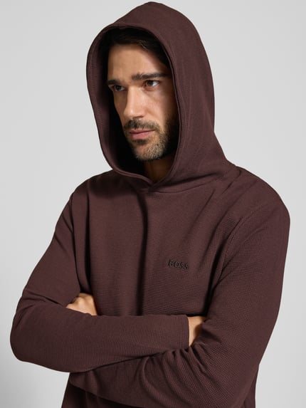 Männermodel trägt Relaxed Fit Sweatshirt aus Baumwoll-Mix Modell 'Waffle LS' von BOSS in Dunkelbraun mit feiner Waffelstruktur, Nahaufnahme Oberkörper, Herren Hoodie von BOSS
