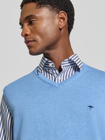 Męski model nosi Regular Fit Pullunder aus reiner Baumwolle mit Logo-Stickerei von Fynch-Hatton, błękit, wyhaftowane logo, dekolt w serek, bez rękawów, ściągacze, 100% bawełna, krój regular fit, długość tyłu w rozmiarze M: 72 cm, zbliżenie na górną część tułowia.