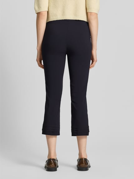 Frauenmodel trägt Caprihose aus Viskose-Mix Modell 'Ina' von STEHMANN in Schwarz, schmaler Schnitt, Drapierungen am Beinabschluss, Rückansicht Ganzkörperansicht. Slim Fit, Bundweite 38 cm, Innenbeinlänge 59 cm, Stretch-Anteil.