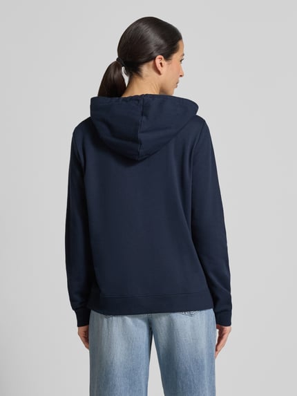 Vrouwenmodel draagt Regular Fit Hoodie aus Baumwoll-Mix van Tom Tailor Denim, effen donkerblauw sweatmateriaal met borduursel, katoenmengsel, lange mouwen, geribde boorden, zijsplitten, kap met trekkoord. Ganzkörperansicht Rückansicht.