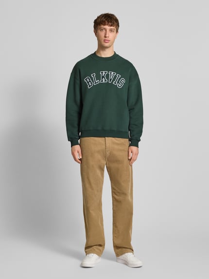 Männermodel trägt Sweatshirt mit Logo und Rundhalsausschnitt von BLKVIS, Reine Baumwolle, Relaxed-Fit, dunkelgrün, Ganzkörperansicht von vorne.