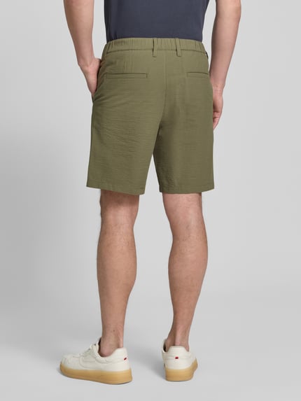 Męski model nosi Regular Fit Bermudas aus Baumwoll-Mix Modell 'KARL' von SELECTED HOMME, efekt: wzór w paski, mieszanka bawełny, krój regular fit, wpuszczane kieszenie, elastyczny ściągacz, szlufki na pasek, zapięcie na guzik i zamek błyskawiczny, faktura seersucker, kolor oliwkowy, Ganzkörperansicht Rückansicht