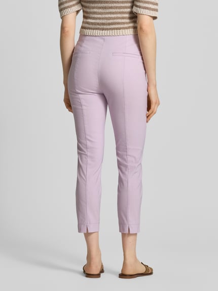 Frauenmodel trägt Slim Fit Stoffhose in verkürzter Passform von Christian Berg Woman, fliederfarben, glatte Textur, Ganzkörperansicht Rückansicht. Elastischer Baumwoll-Mix, Detail Bundweite 39 cm, Innenbeinlänge 66 cm bei Größe 36.