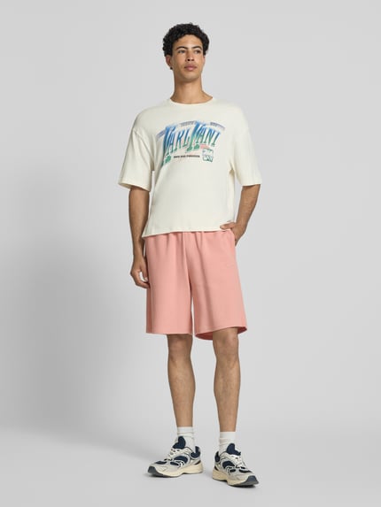 Männermodel trägt Regular Fit Shorts mit Strukturmuster von KARL KANI aus Baumwoll-Mix in Rosa mit Logo-Stitching, elastischer Bund, Ganzkörperansicht von vorne.