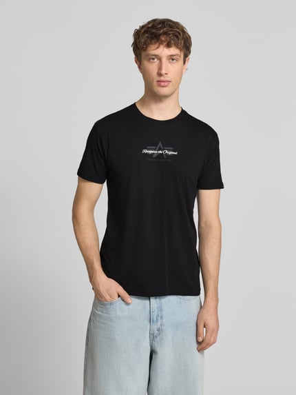 Männermodel trägt Slim Fit T-Shirt aus reiner Baumwolle von Tommy Jeans in Optik: Unifarben mit Label-Print und Logo-Stitching, Ganzkörperansicht von vorne.