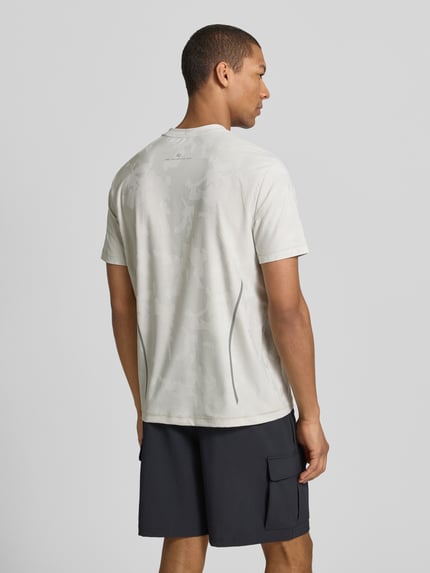 Männermodel trägt T-Shirt mit Rundhalsausschnitt und Label-Detail von EA7 Emporio Armani aus Material-Mix mit Stretch-Anteil, Regular-Fit, Rückenlänge 69 cm bei Größe M, helles Oberteil, dunkle Shorts, Ganzkörperansicht Rückansicht.