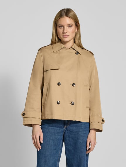 Modelka kobieca nosi Trenchcoat in kurzem Design mit Baumwoll-Anteil od Jake*s Casual w kolorze beżowym, materiał-miks z bawełną, krój prosty, kołnierz klasyczny, podwójny rząd guzików, kieszenie na ręce, pagony na ramionach i rękawach, krótka długość, długość pleców w rozmiarze 36: 64 cm, szerokość ramion w rozmiarze 36: 44 cm, szerokość w rozmiarze 36: 51 cm, długość rękawa w rozmiarze 36: 60 cm, widok na całą sylwetkę od przodu.