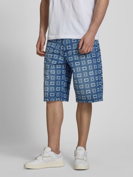 Männermodel trägt Straight Fit Jeans in Denim-Optik mit Allover-Logo-Print von COLUCCI, 5-Pocket-Design, reine Baumwolle, Ganzkörperansicht von vorne.