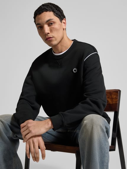Männermodel trägt Sweatshirt aus reiner Baumwolle von Kenzo in Schwarz mit Label-Detail, lockerer Passform, elastischen Abschlüssen, Rundhalsausschnitt, Rückenlänge bei Größe M: 65 cm, Nahaufnahme Oberkörper.